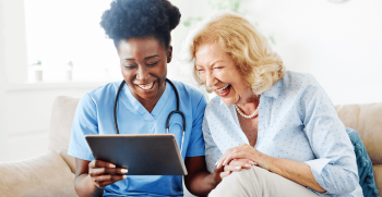 Nurse and older woman smiling looking at ipad.