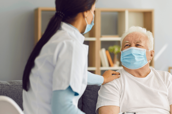 Nurse wearing mask holding the shoulder of an elderly man wearing a medical face mask
