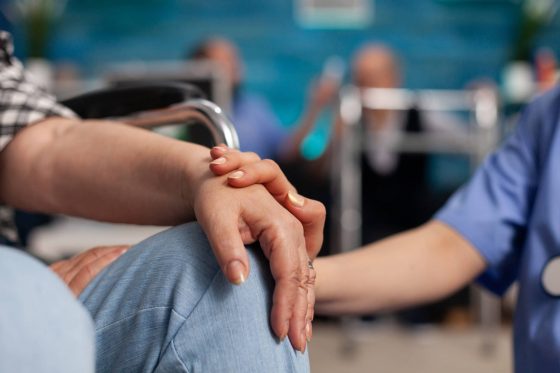 Social assistant worker consoling handicapped pensioner patient touching hands during homecare service. Healthcare support assistance. Social services nursing at home. Caregiver nurse