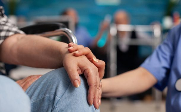 Social assistant worker consoling handicapped pensioner patient touching hands during homecare service. Healthcare support assistance. Social services nursing at home. Caregiver nurse